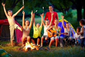 Image of kids and counselor behind a fire pit and in front of a tent at summer camp. 