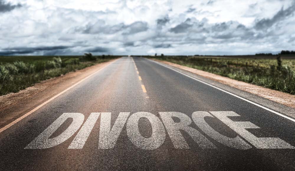 Long straight two-lane road with ominous clouds overhead and the word DIVORCE on the road. 