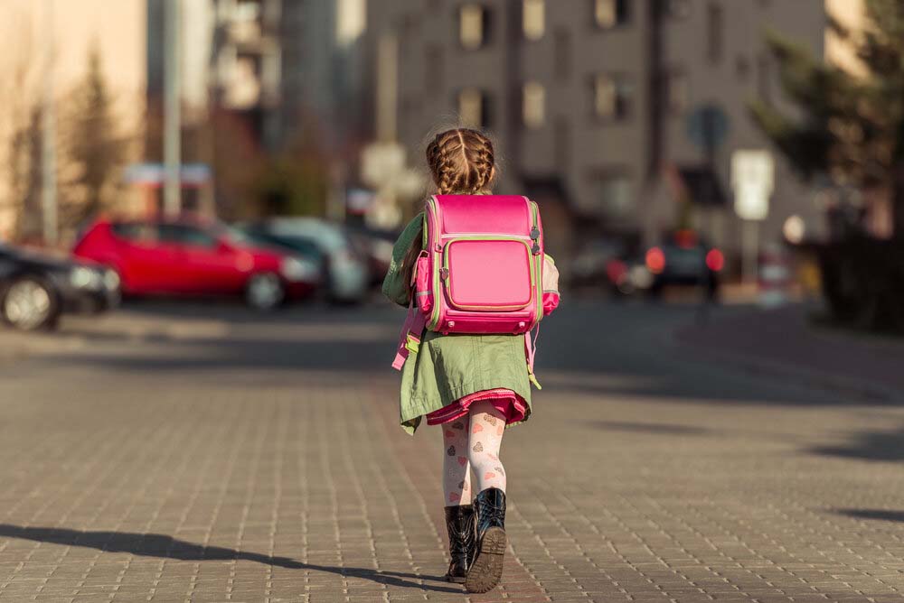 Girl walking down a street with a backpack heading to school.
